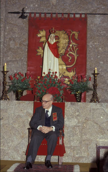 Dr. Plinio em frente ao estandarte de couro sobre parede de pedra.